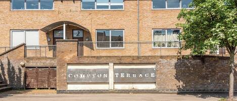 Un edificio de dos pisos con fachada de ladrillo, con el número '2' en la planta baja y un cartel que dice 'COMPTON TERRACE' sobre la entrada.