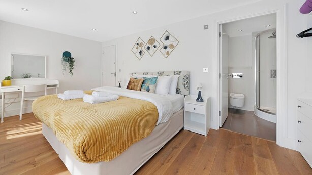 A modern bedroom with a bed, bedside tables, a desk, and a shower area. - Hermitage Rd N4, Manor House | GroundFl | Garden (Greater London)