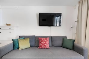 A living room with a grey sofa, a flat-screen TV mounted on the wall, and a white dresser with drawers.