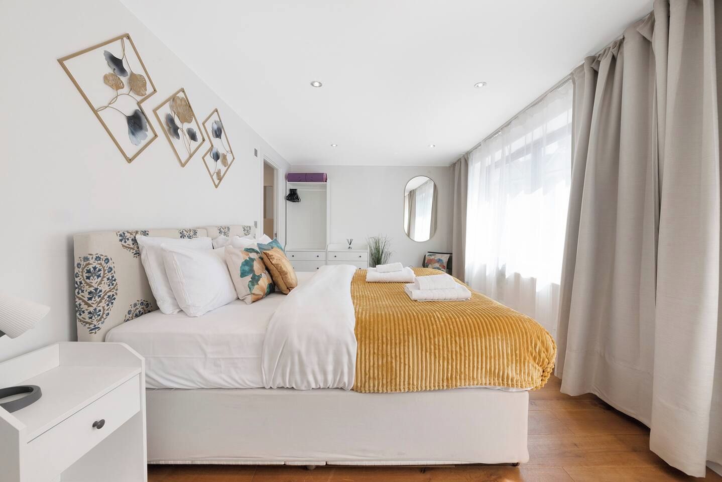 A modern bedroom with a bed, bedside tables, a dresser, a mirror, and a window with curtains.