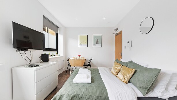 Ein modernes Schlafzimmer mit Bett, Schreibtisch, Stuhl, Fernseher und Wandbildern.