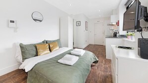 Une chambre d’hôtel comprenant un lit, une table de chevet avec un téléviseur à écran plat, un miroir et une porte donnant accès à une salle de bain.