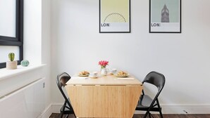 Un coin repas avec une table en bois, deux chaises, une fenêtre ornée d’un cactus et deux tableaux encadrés accrochés au mur.