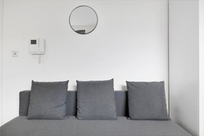 Une chambre à coucher avec un lit, trois oreillers, un miroir rond et un téléphone fixé au mur.