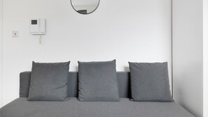 Ein Schlafzimmer mit einem Bett, drei grauen Kissen, einem runden Spiegel und einem an der Wand befestigten Telefon.