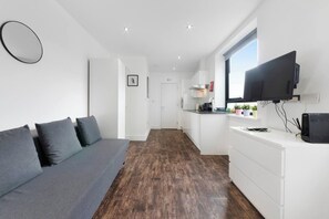 Un espace de vie moderne comprenant un canapé, un téléviseur à écran plat, un coin cuisine et un couloir.