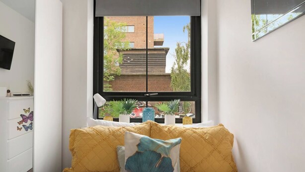 Quarto com cama, janela e vista para um edifício.