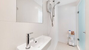 Casa de banho moderna com lavatório branco, chuveiro manual e suporte para rolo de papel higiénico.