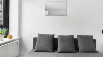 A minimalist bedroom with a bed, two pillows, a small window, and a wall-mounted mirror.