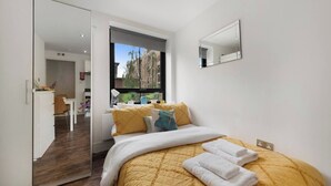 Quarto moderno com cama, mesa de cabeceira, espelho e vista para o exterior.