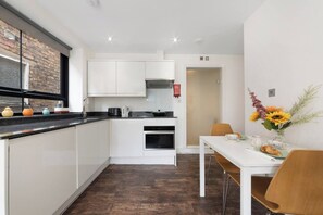 Una cocina compacta con armarios blancos, encimera negra y zona de comedor con mesa y sillas blancas.