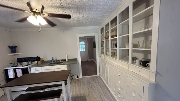 A kitchen with a wooden table, white cabinets, and a ceiling fan.