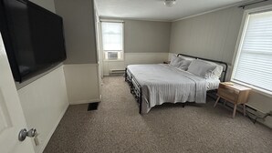 A bedroom with a bed, a TV mounted on the wall, a window with blinds, and a radiator.