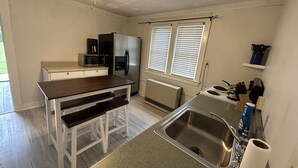 A compact kitchen with a wooden table, a built-in microwave, a stainless steel refrigerator, a sink, and a ceiling fan.