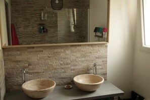 Een badkamer met twee grote, ronde, beige wasbakken op een grijze aanrecht, een spiegel erboven en een muur met een baksteenmotief.