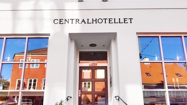 De ingang van CENTRALHOTELLET, met een helder zicht op de gevel van het gebouw, een aantal treden die naar de ingang leiden en potplanten aan de voet ervan.