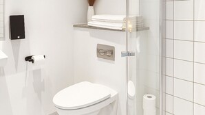 Een moderne badkamer met toilet, een douchecabine van glas, een handdoekrek en een toiletrolhouder.