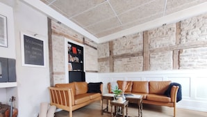 Een gezellige woonkamer met houten vloer, twee bruine leren banken, een klein houten tafeltje met een vaas, en een boekenkast tegen een bakstenen muur.