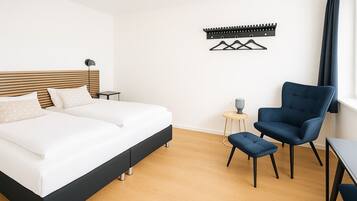 A modern bedroom with a large bed, a blue armchair, a small side table, and a wall-mounted coat rack.