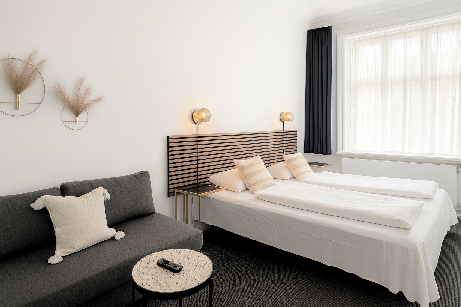 A hotel room with a bed, a sofa, a small round table, and a wall-mounted lamp.
