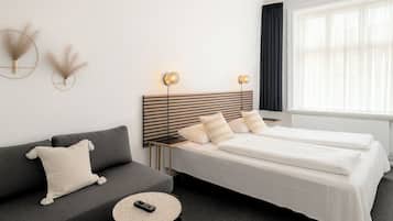 A hotel room with a bed, a sofa, a small round table, and a wall-mounted lamp.