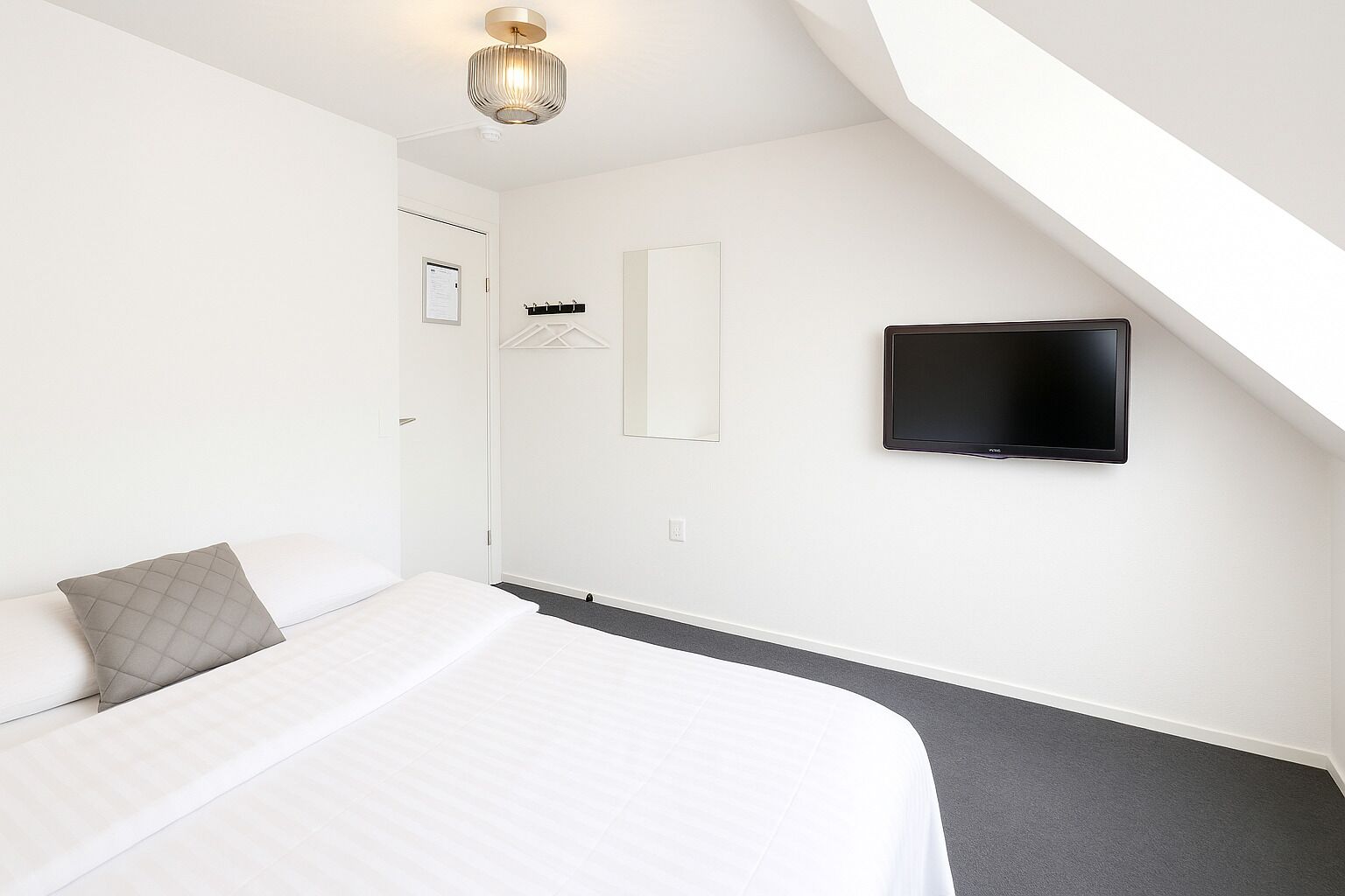 A bedroom with a bed, a television, a light fixture, and a door.