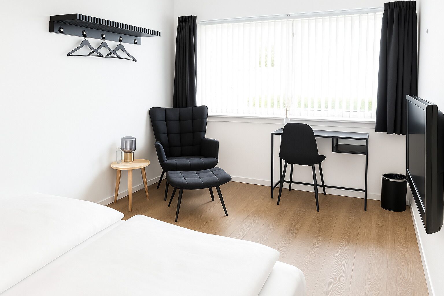 A hotel room with a bed, a desk, a chair, a TV, and a coat rack.