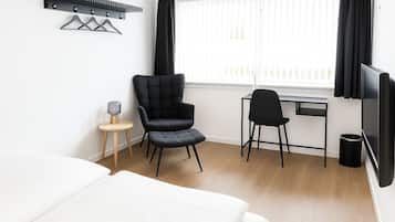 A hotel room with a bed, a desk, a chair, a TV, and a coat rack.