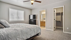 A bedroom with a bed, a ceiling fan, a TV, and a walk-in closet.