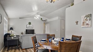 A dining area with a wooden table, chairs, and a sofa. There is a television in the background.