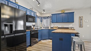 A modern kitchen with blue cabinets, a black refrigerator, and a wooden countertop.