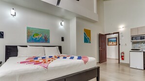 A bedroom with a bed, a bedside table, a nightstand, a wall-mounted lamp, and a painting. - TBS 34A Studio-Garden View-Shared Pool-Beachfront (Placencia)