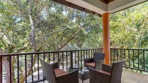 A balcony with wicker furniture, a glass table, and a view of dense foliage. - TBS 34A Studio-Garden View-Shared Pool-Beachfront (Placencia)