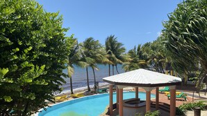 Ein Poolbereich mit Liegestühlen und einem Pavillon, umgeben von Palmen und Blick auf das Meer.