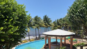 Ein Poolbereich mit Liegestühlen und einer Laube, umgeben von Palmen und Blick auf den Ozean.