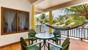 A balcony with a round table and green chairs, overlooking palm trees and a beach. - TBS 39 Beachside-Resort Style Condo-Pool-1 Bedroom (Placencia)