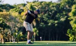 A person playing golf on a course with trees in the background.
