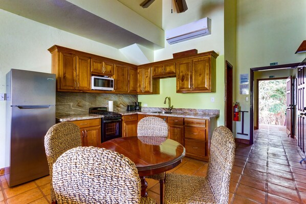 A kitchen with wooden cabinets, a stainless steel refrigerator, a microwave, and a dining table with wicker chairs.