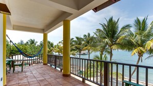 Eine überdachte Terrasse mit einer Hängematte, Blick auf den Strand und Palmen.