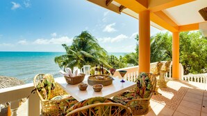 Una terraza con mobiliario de mimbre, una mesa dispuesta con bebidas y aperitivos, y vista al océano.