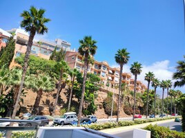 Un hotel de varios pisos con balcones, rodeado de palmeras y un cielo despejado.