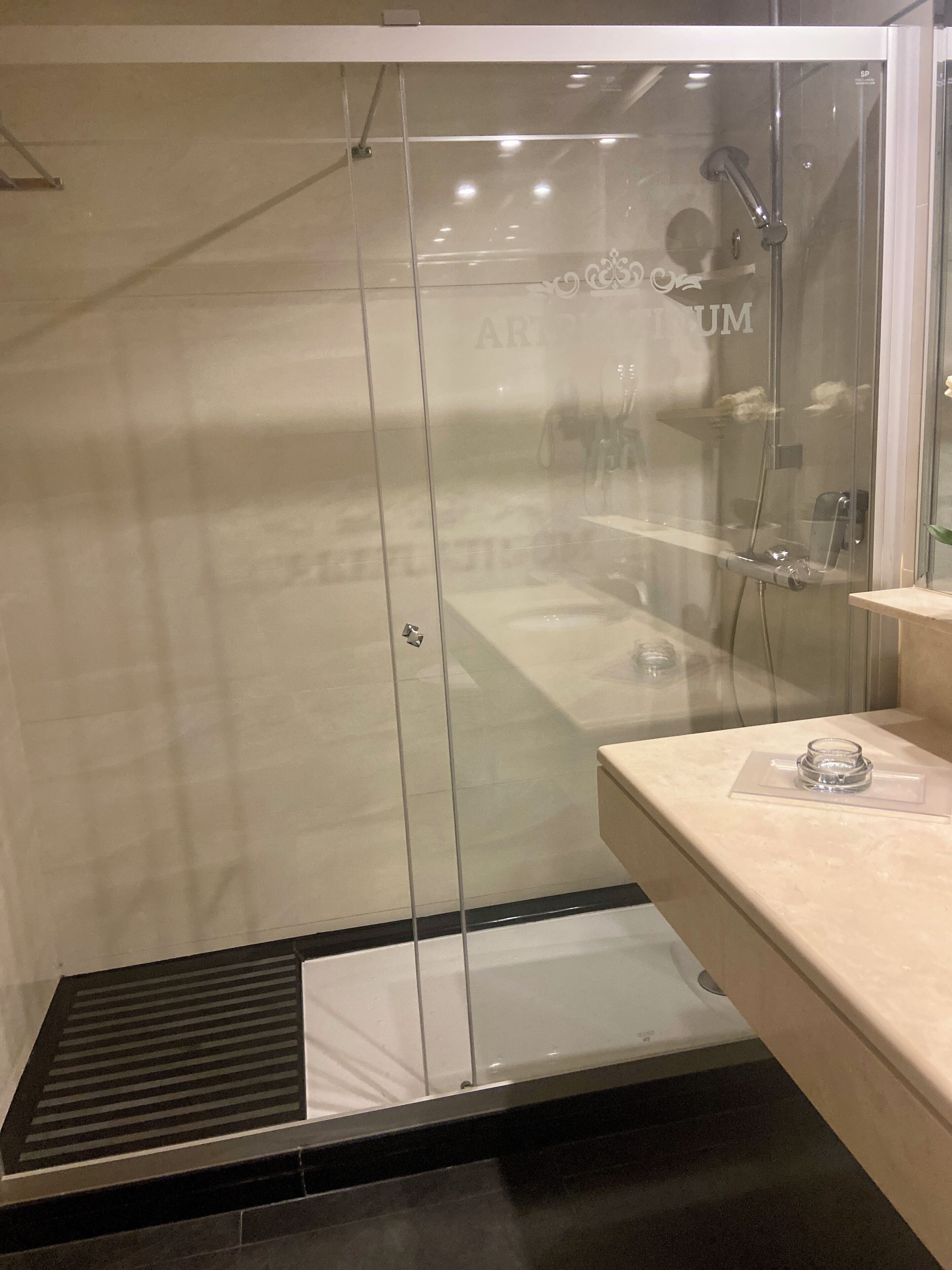 A modern bathroom with a glass-enclosed shower, a marble countertop, and a visible drain.