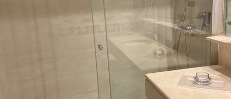 A modern bathroom with a glass-enclosed shower, a marble countertop, and a visible drain.