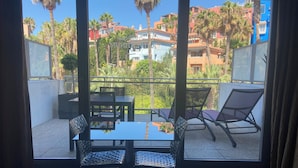 A balcony with two chairs and a table, overlooking a residential area with palm trees and colorful buildings. - Artplatinum Suites & Apartments (Benalmádena)