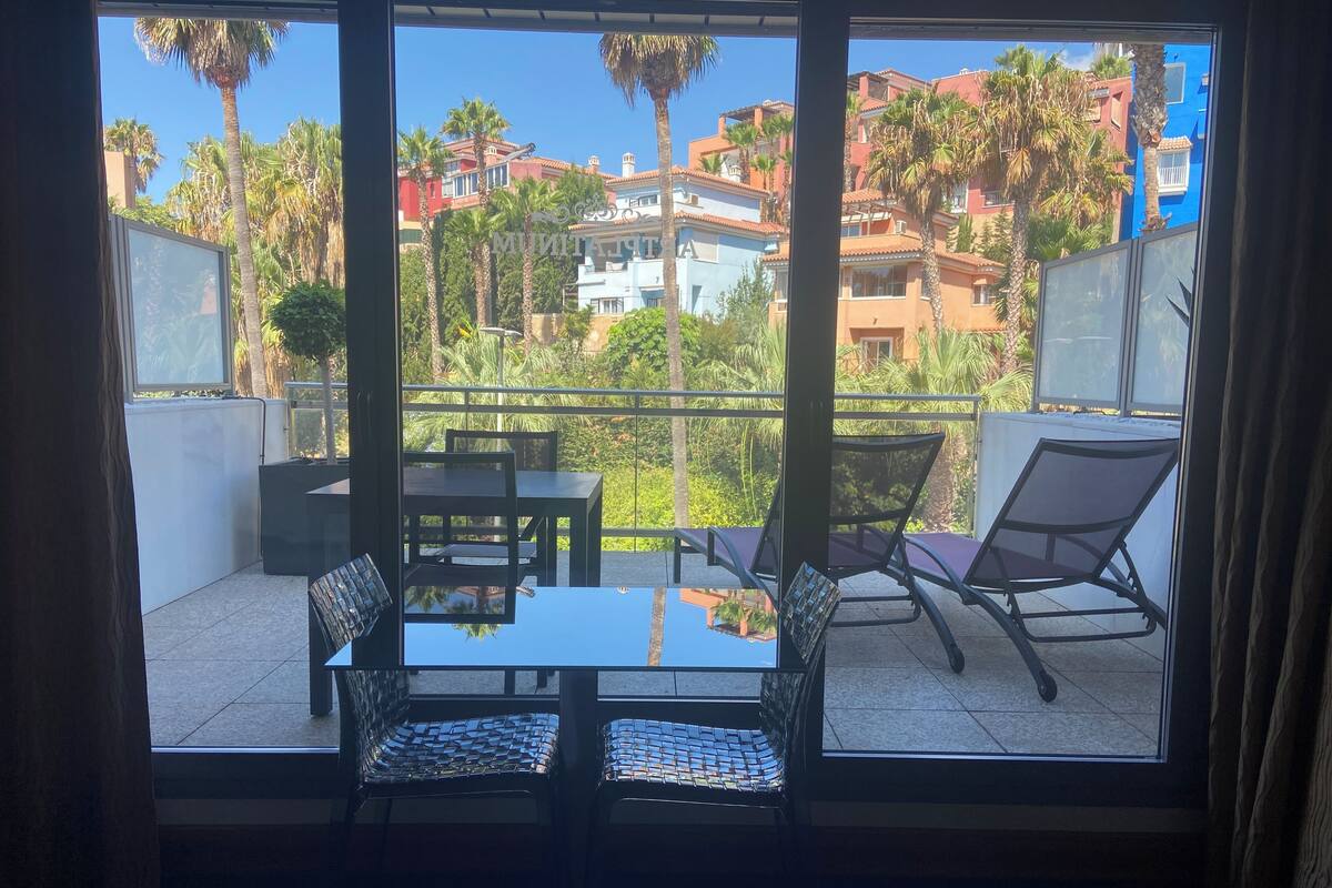 Ein Balkon mit zwei Stühlen und einem Tisch, mit Blick auf eine Wohngegend mit Palmen und bunten Gebäuden.