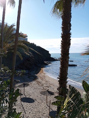 Una spiaggia con una scogliera rocciosa, palme e un cielo azzurro limpido.