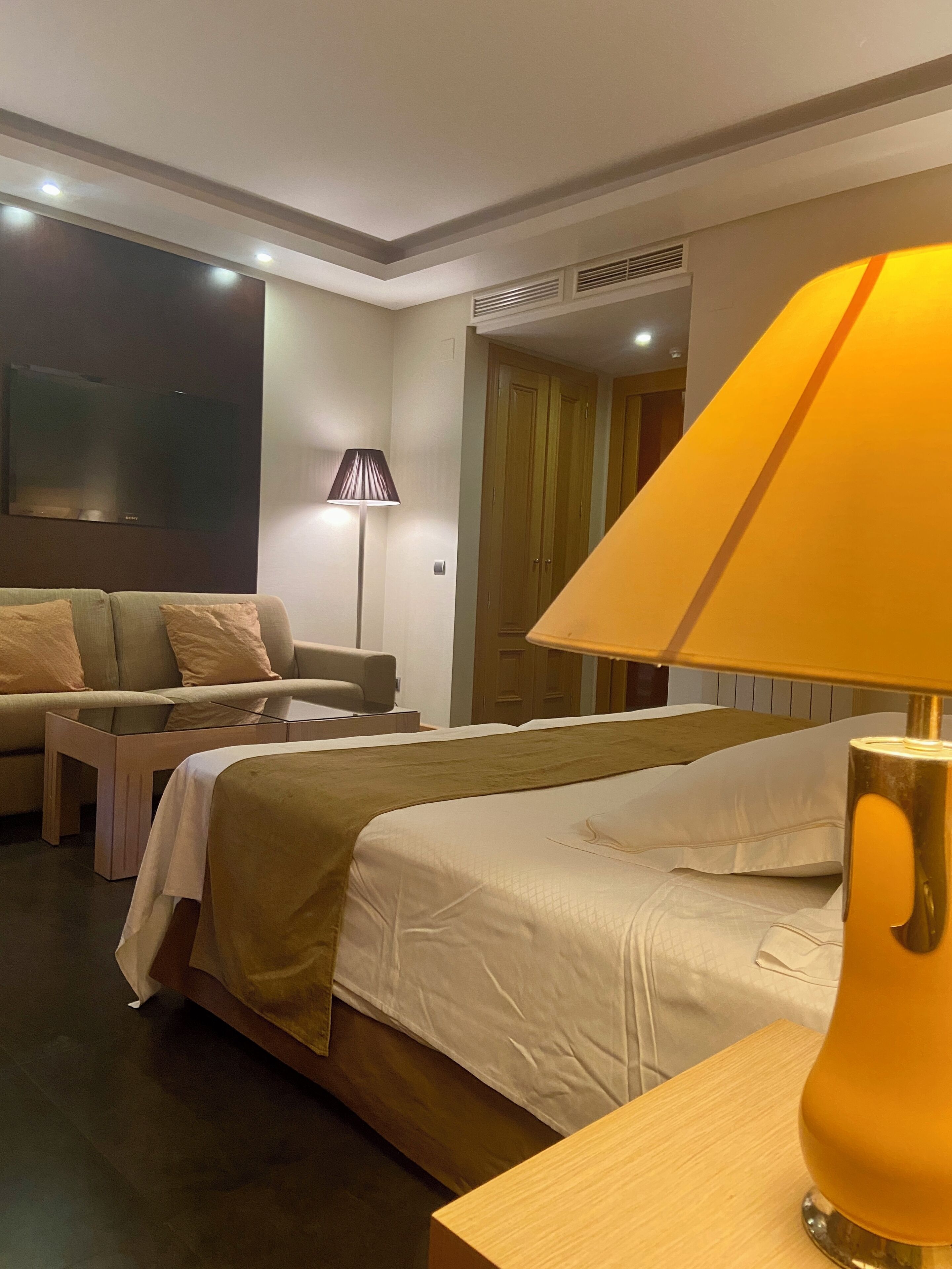 Una habitación de hotel con cama, sofá, lámpara y televisor.