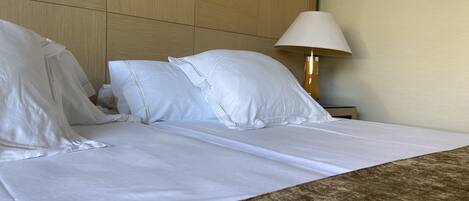 A hotel room with a bed, pillows, a lamp, and a headboard.