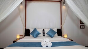 Cama bem arrumada com colcha azul, duas almofadas e toalhas enroladas ao centro.