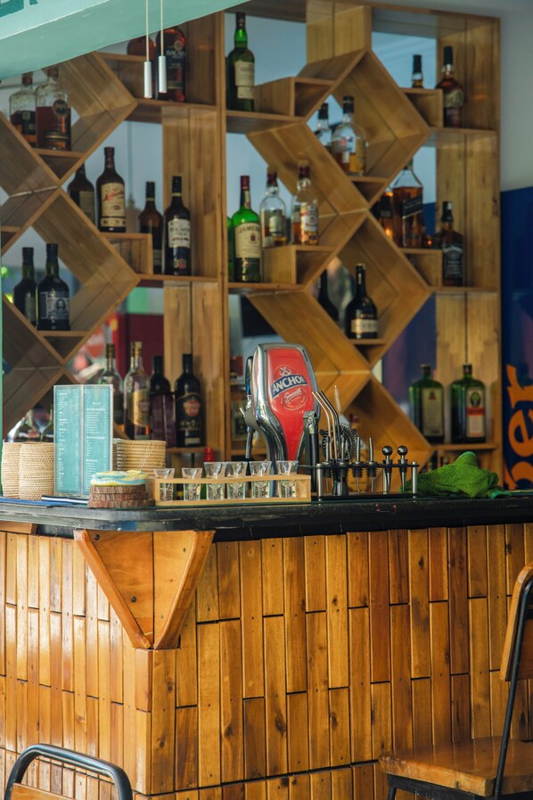 A bar area with wooden shelves stocked with various liquor bottles, a cash register, and bar tools.